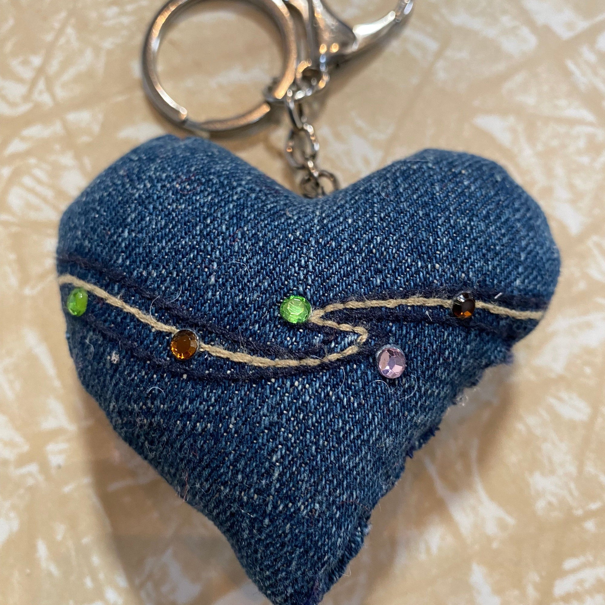Blue denim keychain with floral embroidery on a textured beige background_Transmutation-keychain.