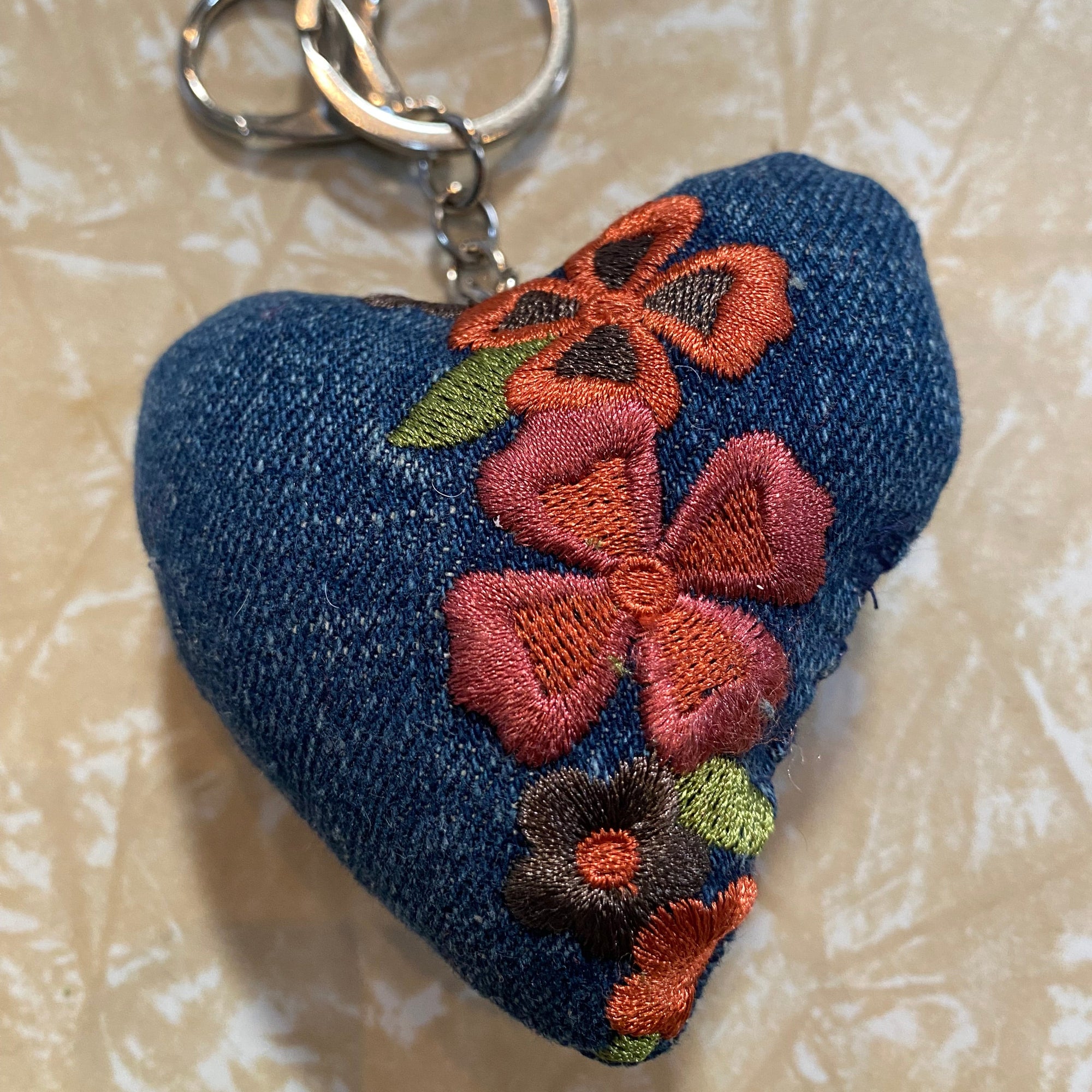 Blue denim keychain with floral embroidery on a textured beige background_Transmutation-keychain.
